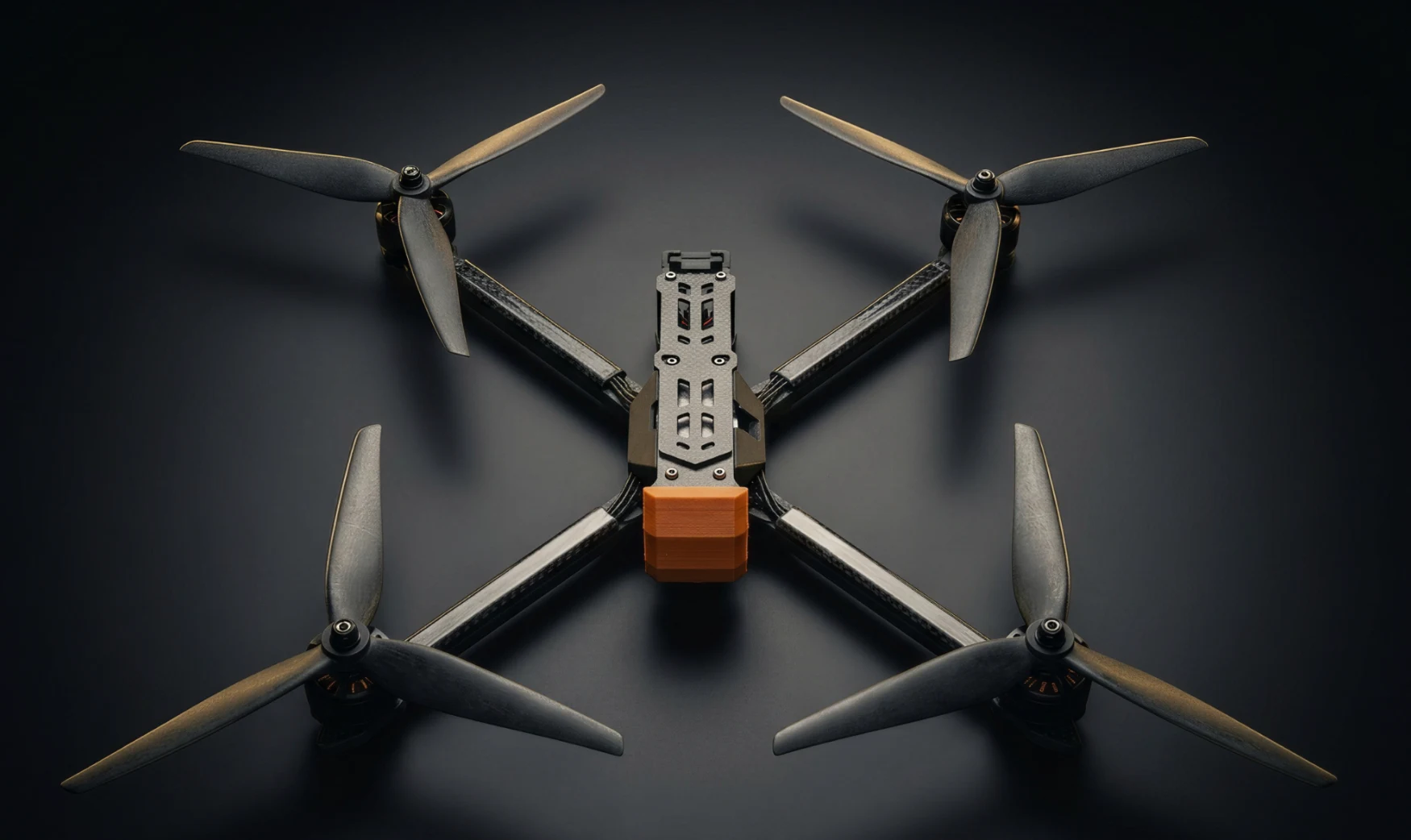 Unmanned Industries T100 FPV airframe, top-down studio shot lit with gold rim light on a near-black background